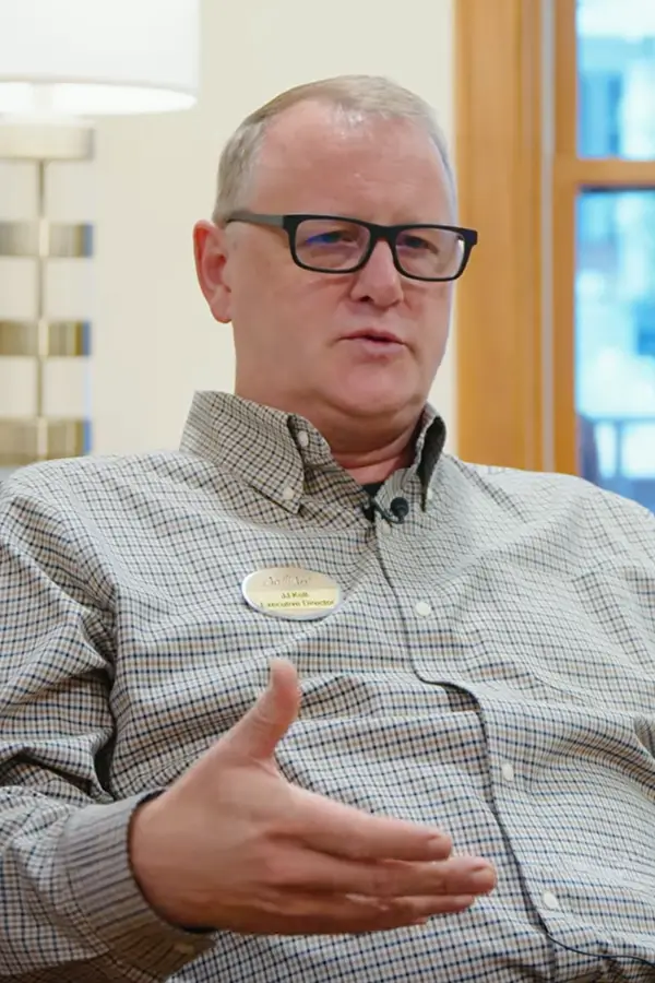 A white male wearing a button down shirt, in the midst of giving an interview response